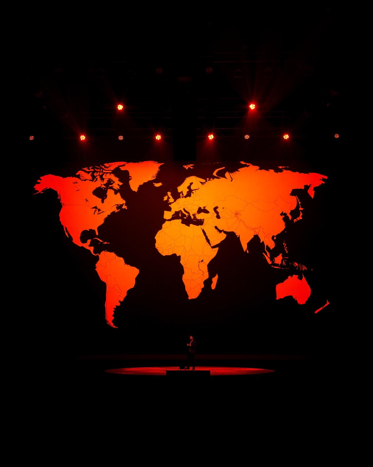 Speaker on stage in front of a giant illuminated world map